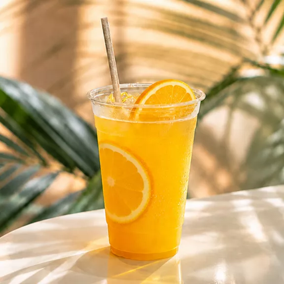 A clear plastic cup filled with bright orange juice sits on a light-colored surface.