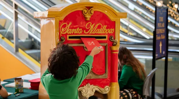 A child putting a red letter into Santa's Mailbox at Brightline station