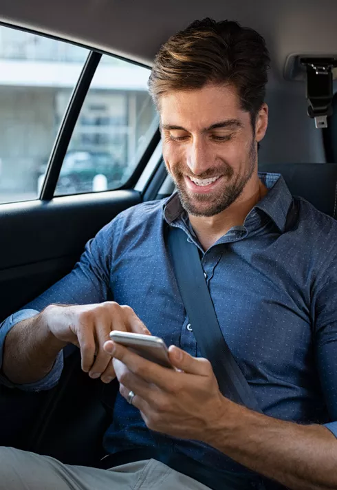 A guest buckled in the back seat of a ride share vehicle scrolling on their phone