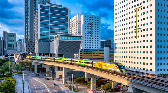 A train departing the Brightline MiamiCentral station exterior with surrounding buildings and street in view 