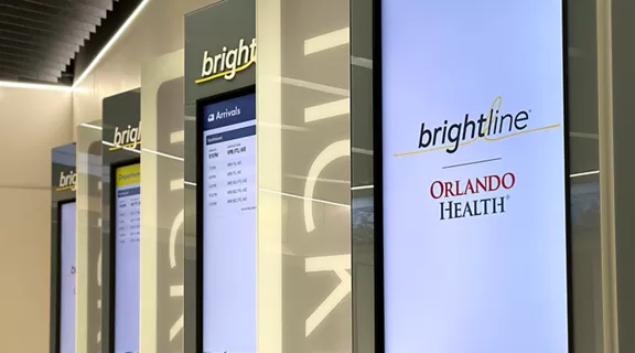 Four Brightline kiosks in a row with Brightline and Orlando Health logos on screen