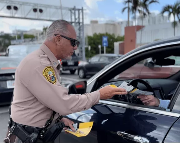 A police officer hands out safety information at a Brightline crossing.