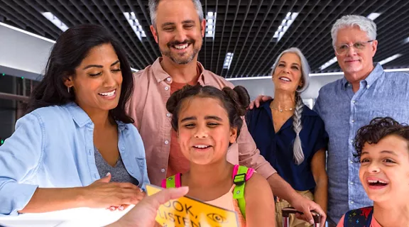 A family of six smiling at off camera person holding a flyer in Brightline Orlando station 