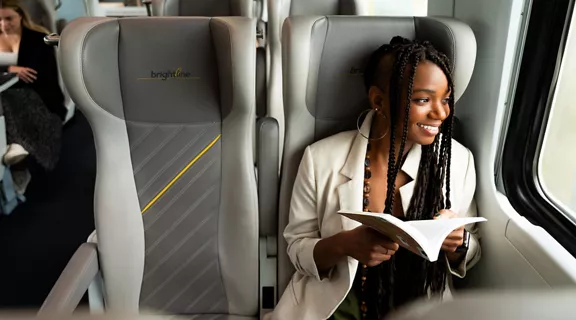 A young woman sitting on a Brightline train looking out the window