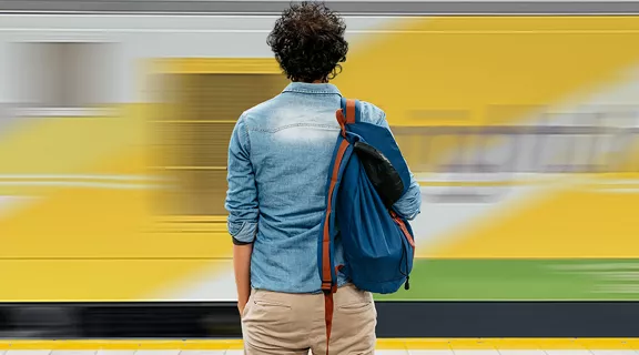 Student with backpack standing on a station platform facing a moving Brightline train as it passes by.