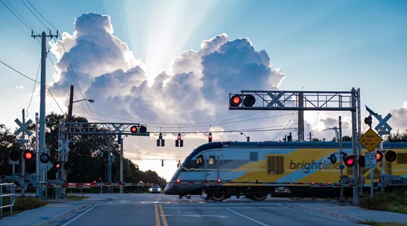 A Brightline train traveling through a rail crossing at dawn. 