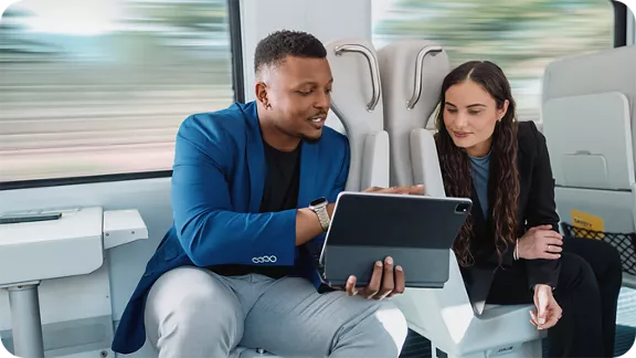 A man showing his laptop screen to a young lady while riding on the Brightline train