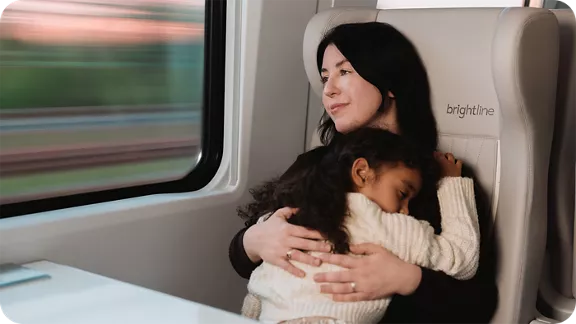A mother holding her daughter while she looks out the window on the Brightline train
