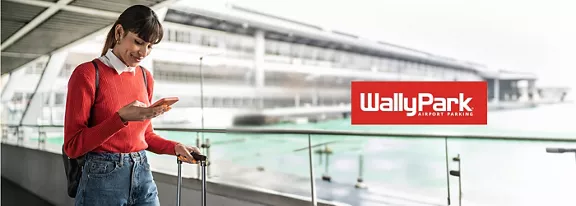 A woman on the go with her rolling suitcase in one hand and looking down at her phone in the other, A WallyPark logo over-layed to the right