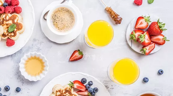 Flat lay with scotch pancakes in flower form, berries and honey with human hands. Healthy breakfast concept. Women eating together, top view.