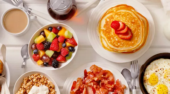 A brunch table with plates of pancakes, eggs, and fruit.