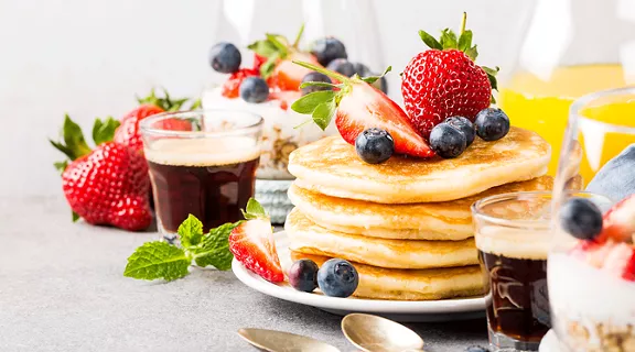 A brunch table with stacks of pancakes, cups of coffee, and fruit