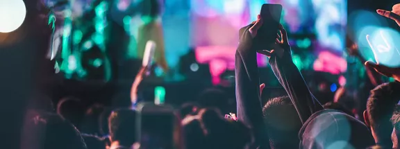 A crowd, surrounded by blue and pink concert lights, taking pictures of a concert on their phones