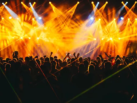 Crowd is enjoying live performance at open air summer festival at night. Nightlife. Silhouettes of people are standing in the dark and listening to electro music at concert. There are orange lights.
