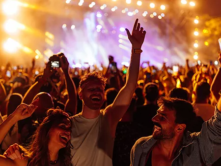 Group of young friends partying and celebrating at summer music festival. They are dancing in front of stage. Wearing casual clothing