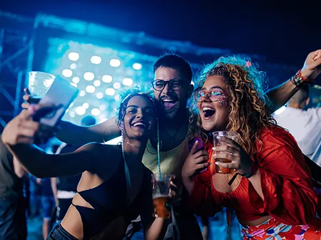 A small group of friends are at a music festival taking a selfie together with excited expressions on their faces.