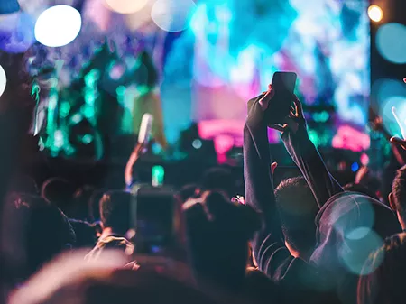 A crowd, surrounded by blue and pink concert lights, taking pictures of a concert on their phones