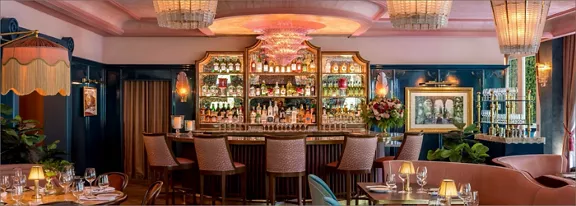Upscale cocktail bar interior featuring a central backlit bar with an extensive display of bottles a