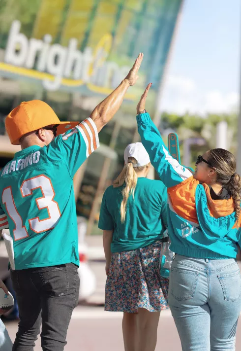 Two Miami Dolphins fans giving each other a high five outside a Brightline train station.