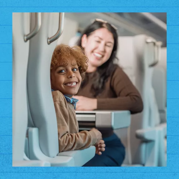 A young child smiles brightly while seated on a modern train.