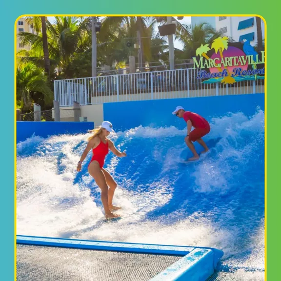 Two surfers in red swimsuits ride artificial waves at a Margaritaville Beach Resort attraction.