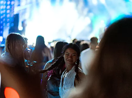 Two Asian and Caucasian girls dance in the crowd and enjoy the atmosphere at a music festival.