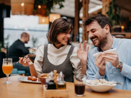 A man and woman laughing while sharing food and drinks at a brewery