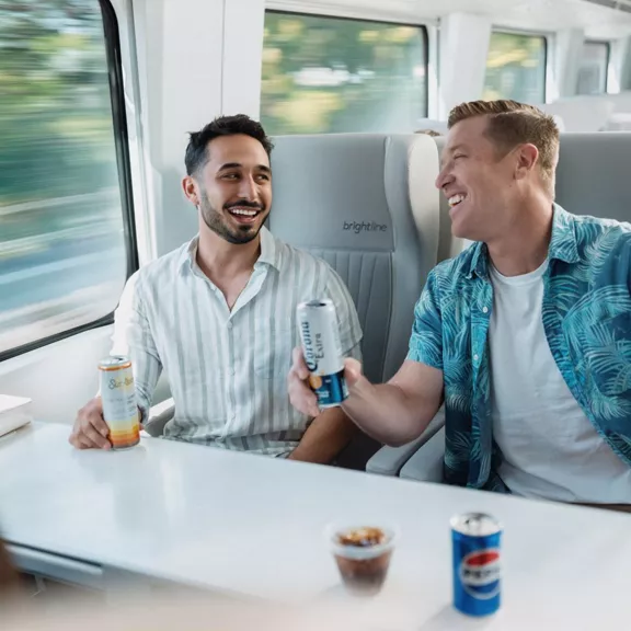 two guys seated on a train holding drink cans