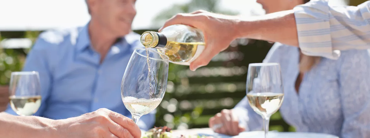 Hand pouring wine into glass and people seated around table