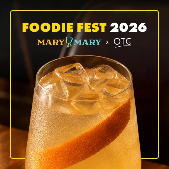 Promotional graphic for Foodie Fest 2026 featuring a close-up of a chilled cocktail. The drink is served in a clear glass filled with ice cubes and a large slice of citrus peel. 