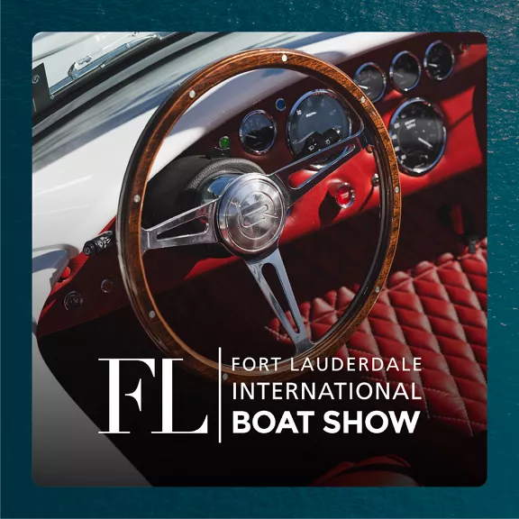 Close-up of a classic boat steering wheel with a wooden rim and metallic spokes. The dashboard features multiple round gauges set against a glossy red panel. 