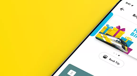 A smartphone displays the Brightline Wallet app interface, featuring a digital card with the words Happy Birthday brightline and colorful presents and train image. The app screen shows options such as 'Book Trip' and informational text. The phone is set against a vibrant yellow background.