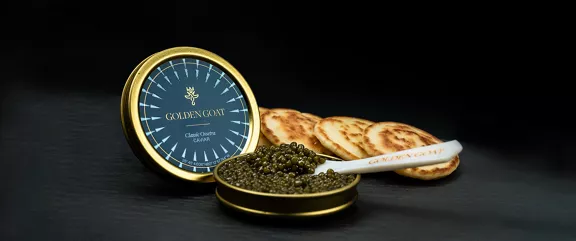 An opened tin of Golden Goat caviar with a serving spoon and round crackers