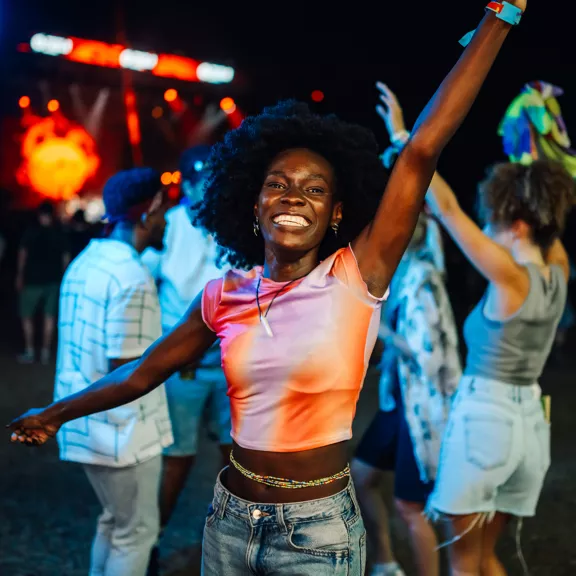 A young woman smiles brightly while dancing at an outdoor night music festival.