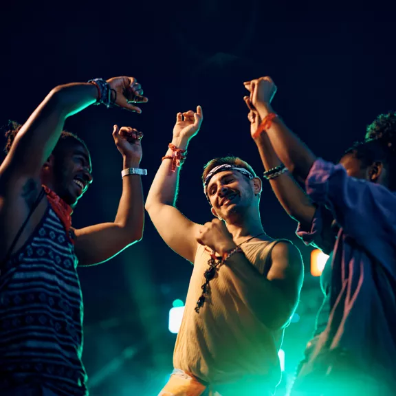 A group of young adults dance together under vibrant stage lights at an outdoor night event.