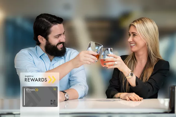 Couple toasting with glasses with Brightline Rewards logo