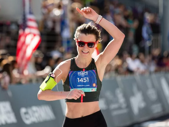 A woman cheering as she crosses the finish line at the Miami Marathon.