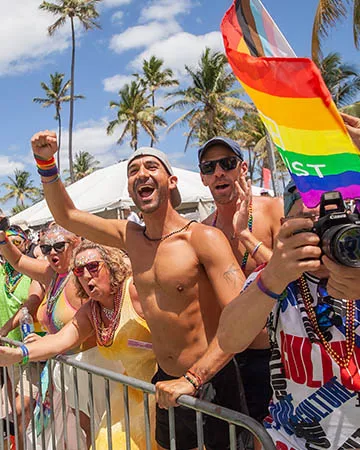 Pride attendees cheering on the sidelines with a rainbow flag