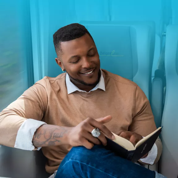 A man reading a book while taking a ride on a Brightline train.