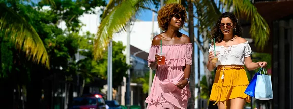 Female friends holding shopping bags and drinks in city. Young women are walking on street during summer. They are enjoying city life on sunny day