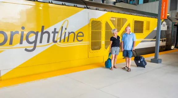 A couple standing on a Brightline train platform with a Brightline Train behind them