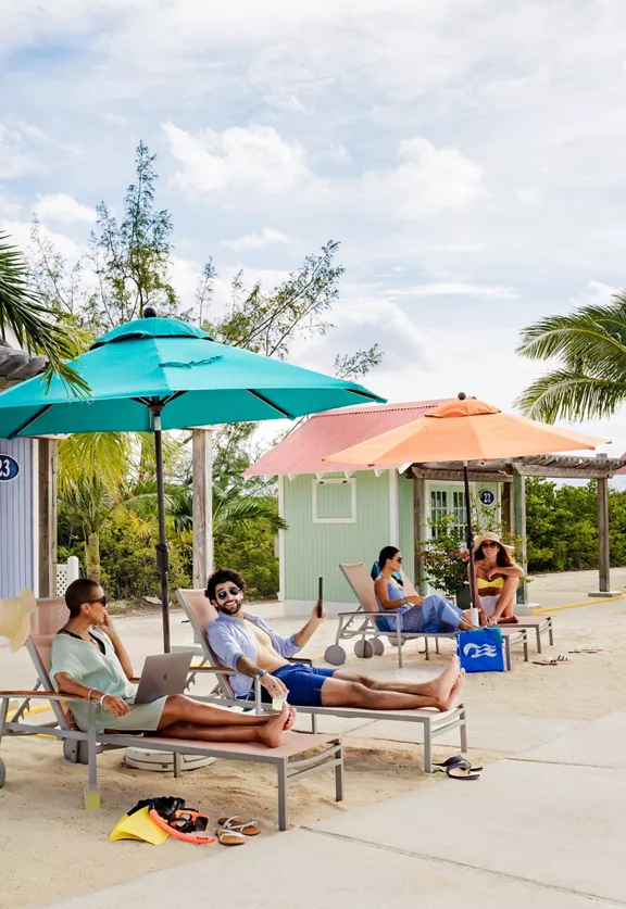 Two groups of two people sitting on lounge chairs under umbrellas.