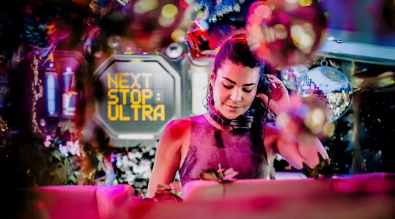 A female DJ playing music, surrounded by neon festival lights