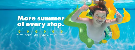 A boy giving two thumbs up underwater at a pool.