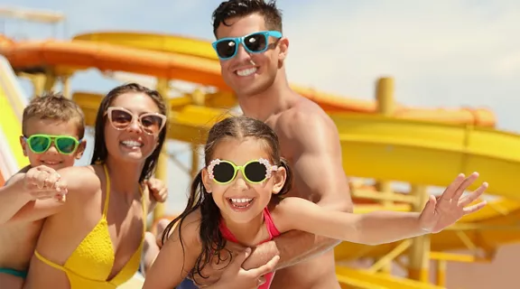 Two women sharing an ice cream at a theme park, with a carousel shown inA mom and dad posing for a photo with their two children at a water park. the background