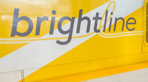 A couple standing on a Brightline train platform with a Brightline Train behind them