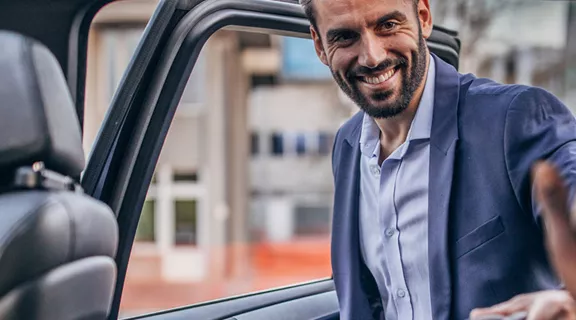 A Guest entering a rideshare vehicle smiling at the passanger already in the vehicle