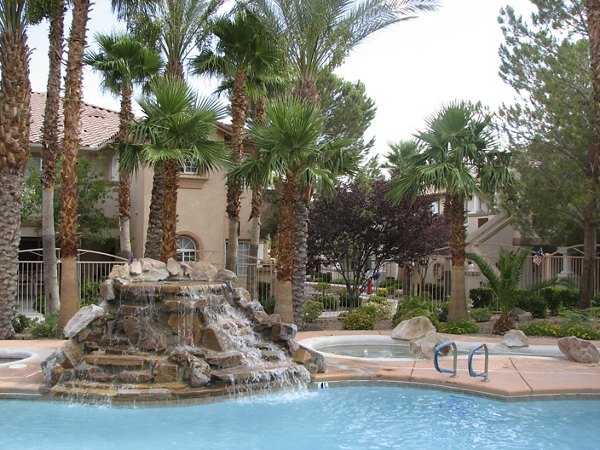 Resort-style pool area with lounge chairs and palm trees at Destinations Pueblo Apartments