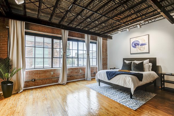 Cozy bedroom with exposed brick and large windows in Mitchell Lofts, featuring modern luxury apartment design in Dallas