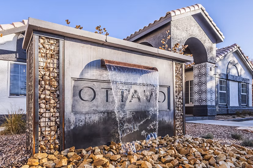 Decorative water feature with Ottavo surrounded by rocks in front of an arched building with a tiled roof